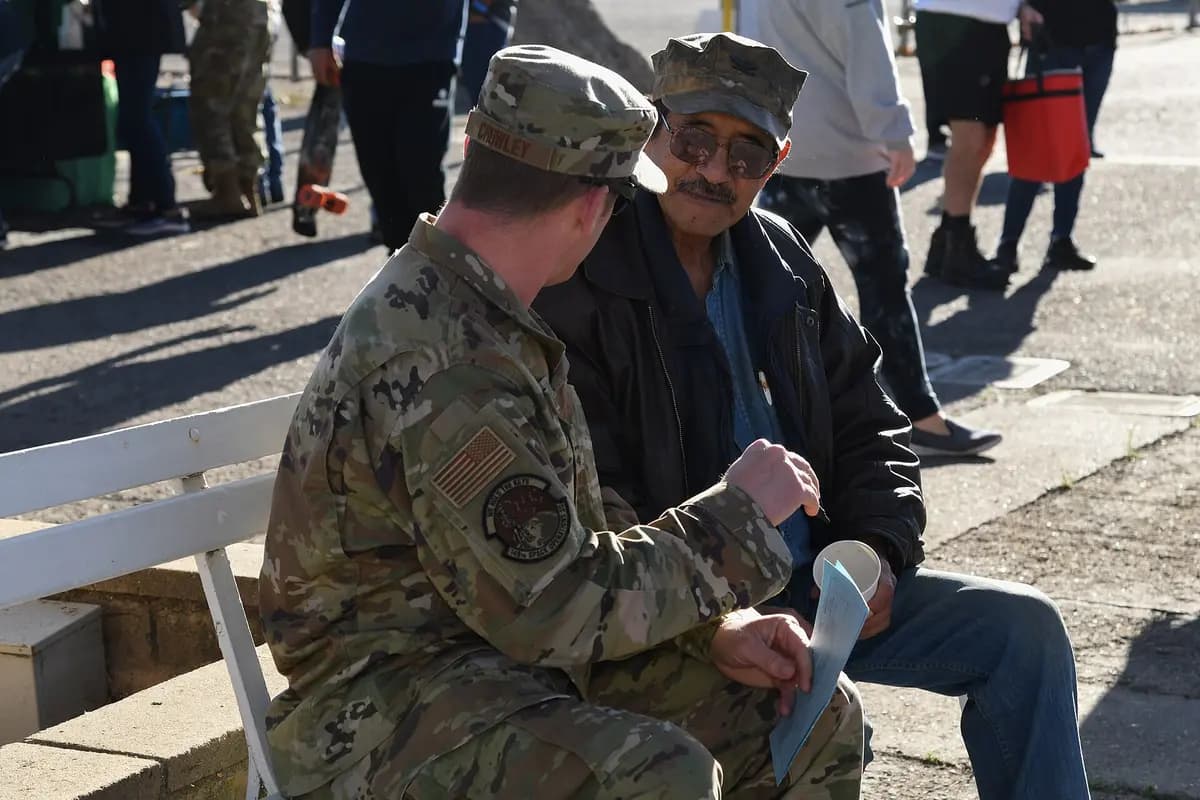 An airman sitting on a bench talking one-on-one with an older veteran at a community stand down event